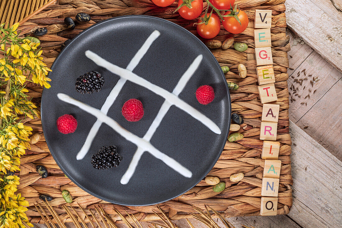 Top view of noughts and crosses game concept on plate with fresh blackberries and raspberries between whipped cream near inscription