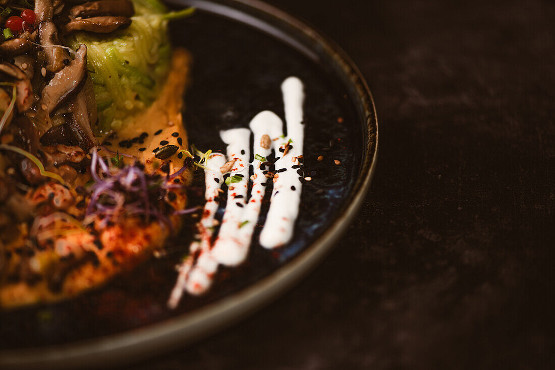 Close up crop view of yummy vegan dish with zucchini spaghetti and sauteed mushroom slices covered with red berries and alfalfa sprouts on dark background