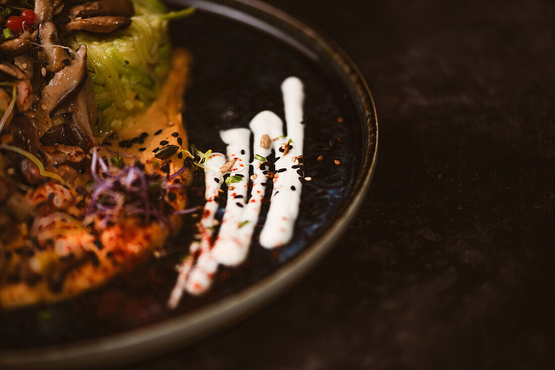 Nahaufnahme eines leckeren veganen Gerichts mit Zucchini-Spaghetti und sautierten Pilzscheiben, bedeckt mit roten Beeren und Alfalfa-Sprossen auf dunklem Hintergrund