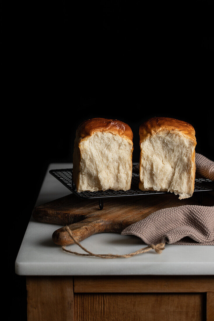 Delicious split halves of sandwich bread on grill tray placed on counter and cutting board against dark background