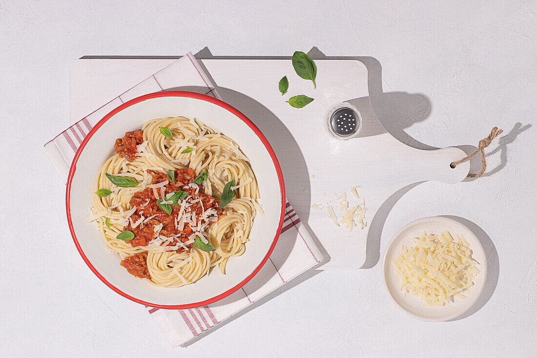 Draufsicht auf einen Teller mit Spaghetti Bolognese mit Tomatensauce auf weißem Tischhintergrund