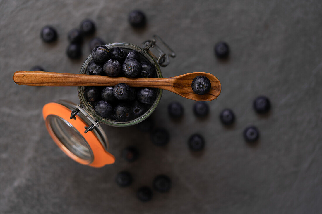 Fresh blueberries falling in glass jar and splashing water on gray background in studio
