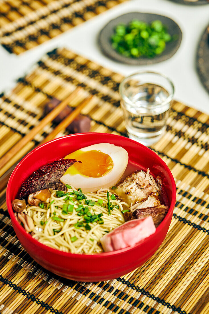 From above of appetizing ramen soup with meat and egg and noodles served in bowl on table near chopsticks and glass cup