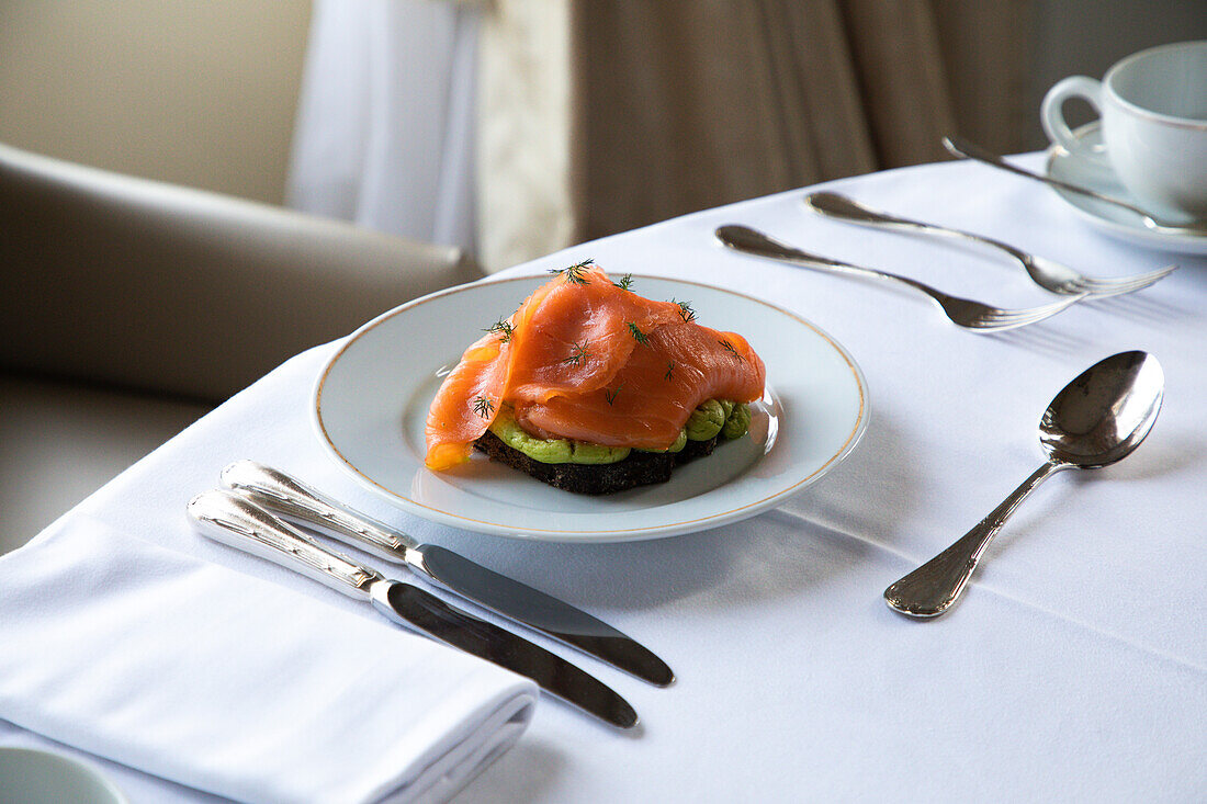 High angle of plate with delicious avocado toast with poached egg and smoked salmon served on table with cutlery and coffee cup during breakfast in hotel restaurant
