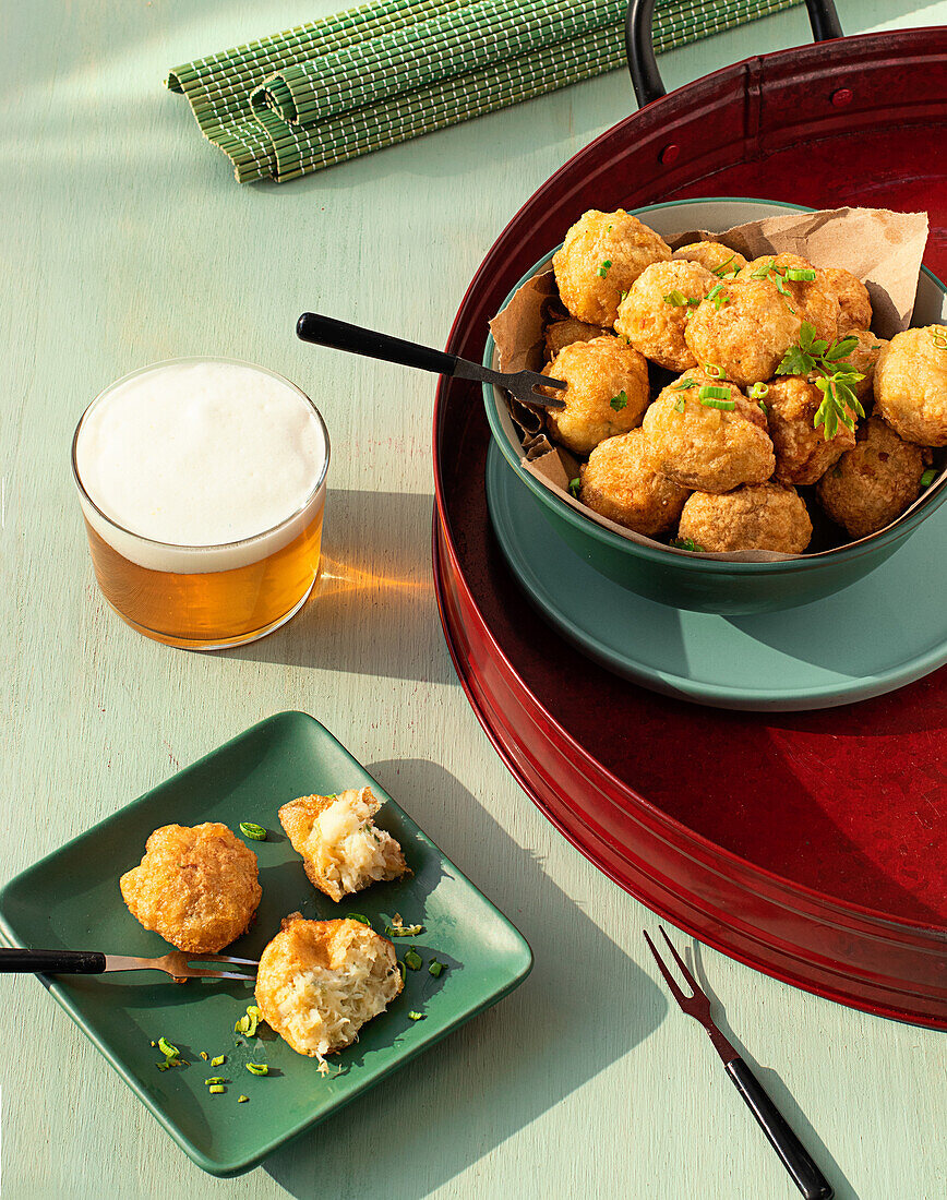 From above traditional codfish fritters server on tray with fresh herbs and glass of beer on green background