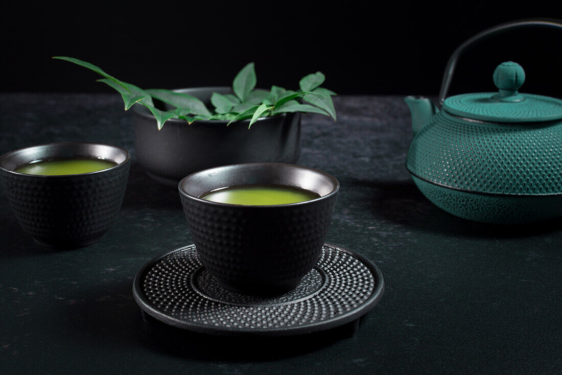 Schwarze Keramiktasse mit traditionellem japanischen grün gefärbten Matcha-Tee, serviert auf einem Tisch mit Teekanne