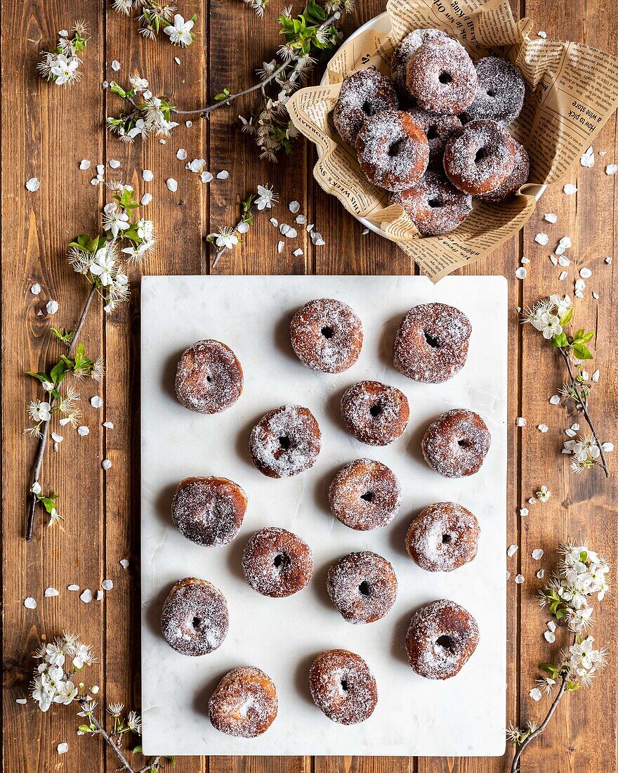 Draufsicht auf appetitanregende geliehene Donuts, die auf einer weißen Tafel auf einem Holztisch mit Blumen angeordnet sind
