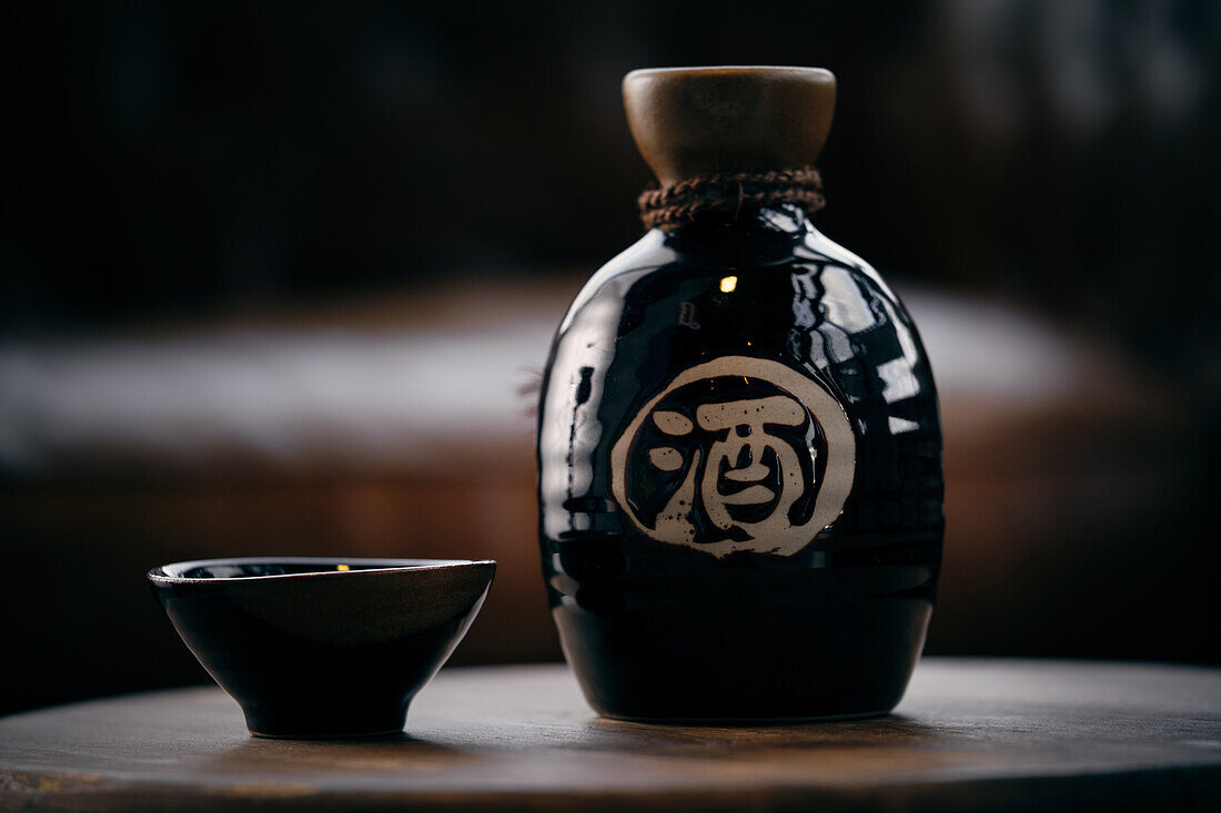 Black ceramic bottle and small bowl with soy sauce placed on wooden table