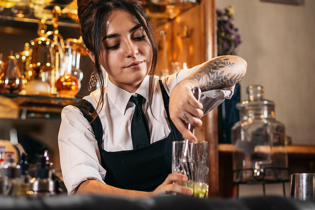 Barkeeper mit Muddler beim Mischen eines erfrischenden Cocktails in einem Glas mit Eis und Limette während der Arbeit im Pub