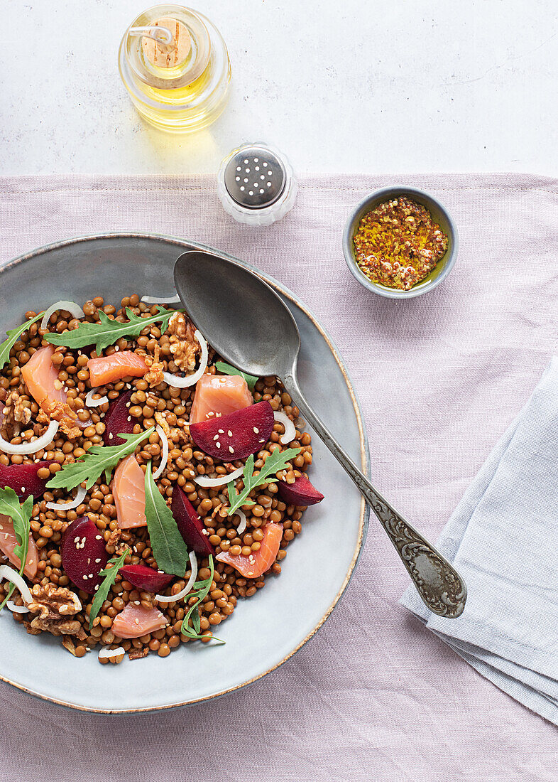 Nahaufnahme eines Lachs- und Linsensalats von oben auf einem Tisch mit rosa Tischtuch