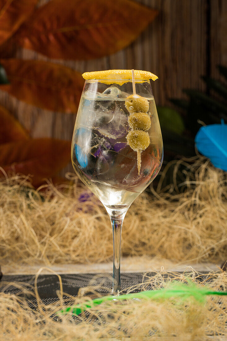 Crystal wineglass with Martini cocktail served with lemon zest and olives edge placed against dry grass