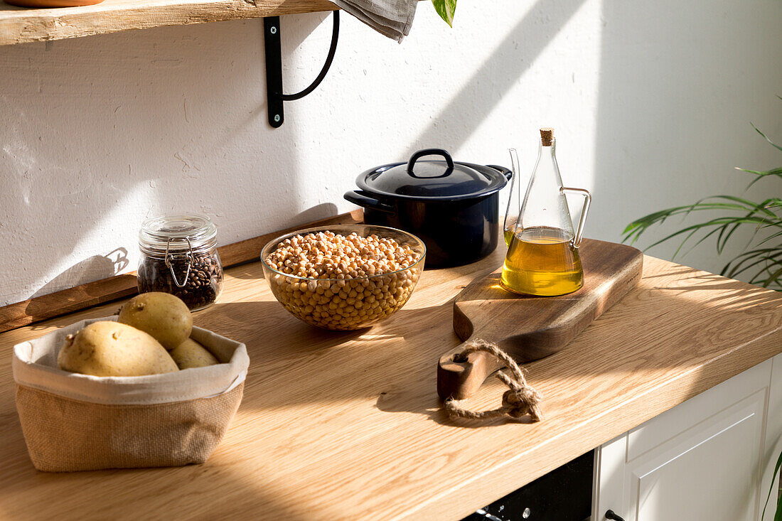 Verschiedene Zutaten und Utensilien auf einem Holztisch während des Kochvorgangs in einer Küche mit weißen Wänden und minimalistischem Interieur im natürlichen, umweltfreundlichen Stil