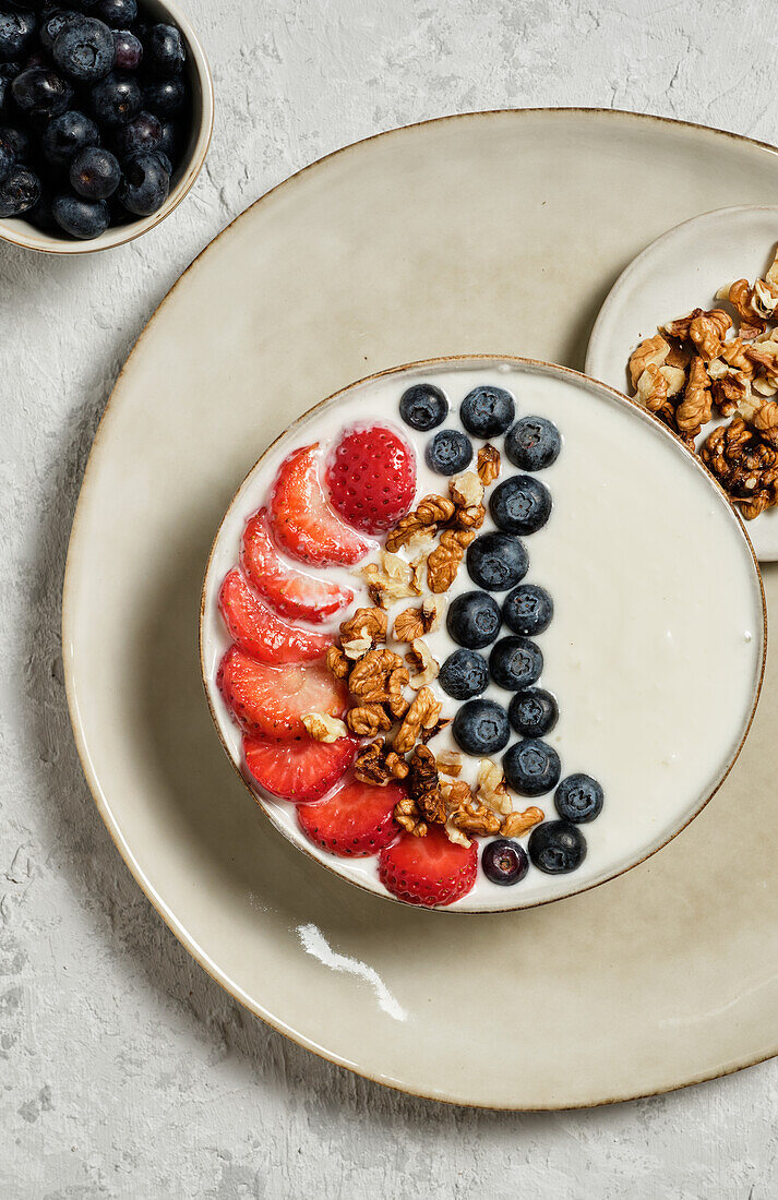 Draufsicht auf eine leckere gesunde Frühstücksschüssel mit weißem Joghurt und frischen Erdbeeren und Blaubeeren mit Müsli