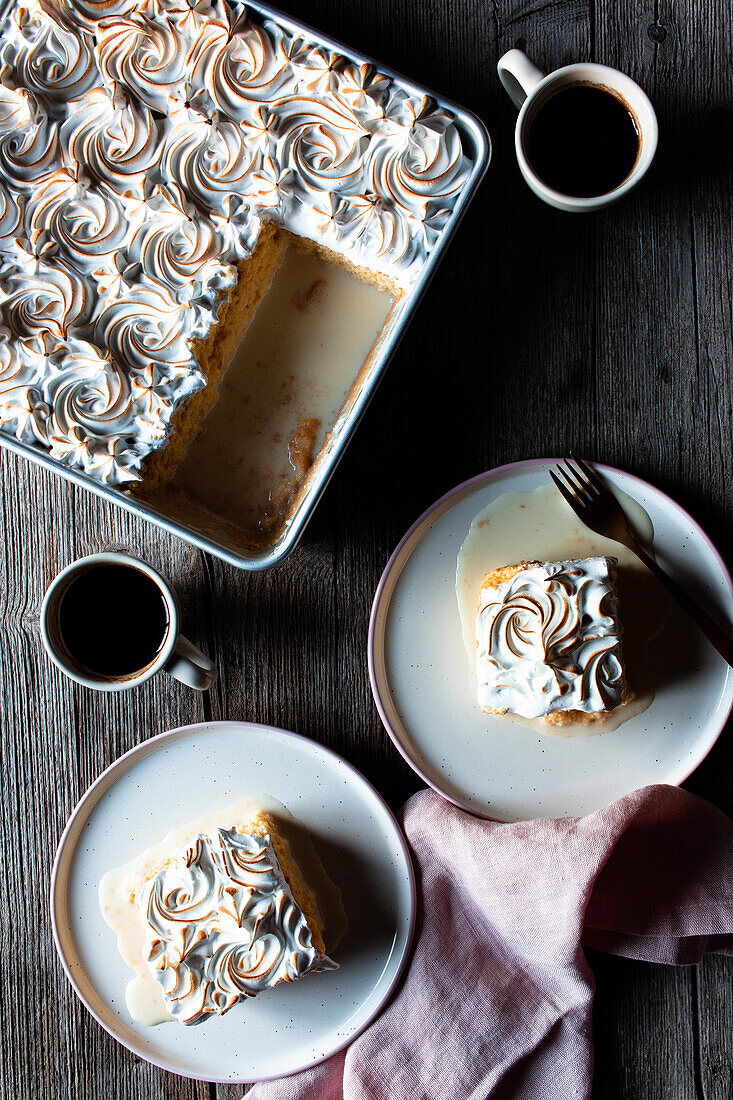 From above three milks cake in baking dish and plates with cups of strong coffee on wooden table
