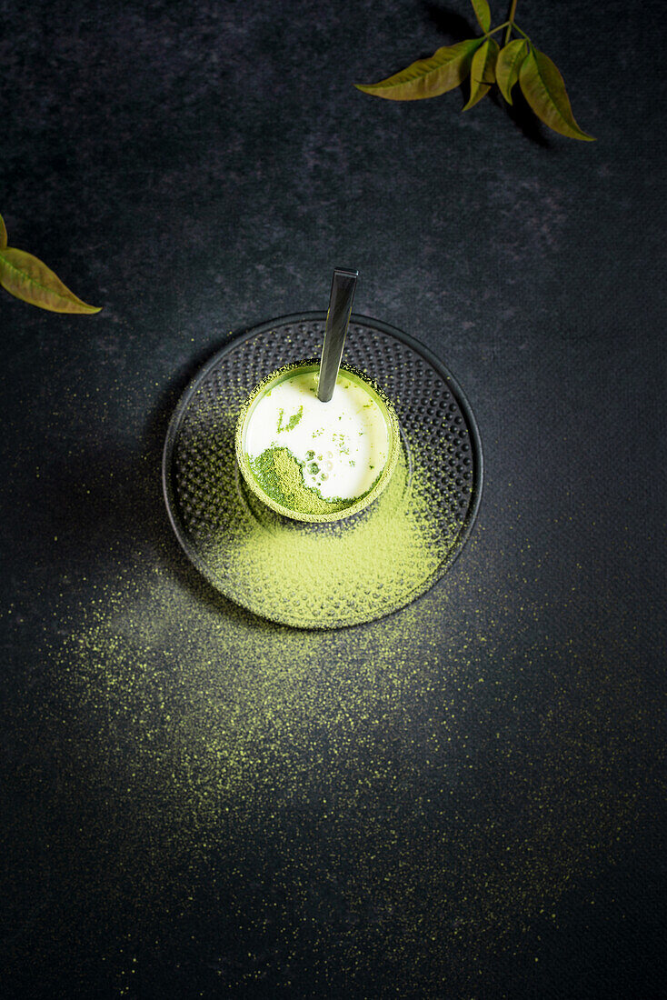 High angle of glass with cold green matcha latte with milk served with straw on saucer on black table