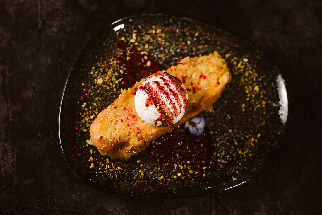 Draufsicht auf leckeren French Toast mit Baiser-Milch-Eiskugel, bedeckt mit süßer Beerensauce auf einem Teller mit Gewürzen in einem Restaurant auf dunklem Hintergrund