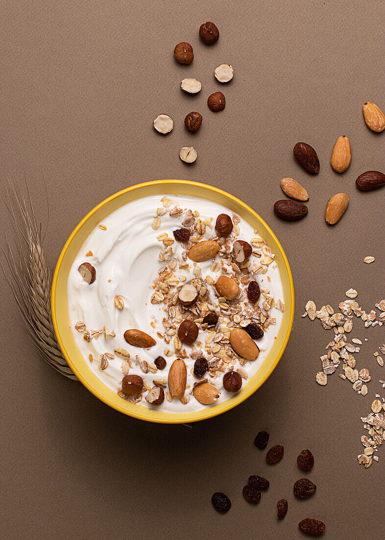 Joghurt von oben mit Haferflocken und getrockneten Nüssen auf braunem Hintergrund