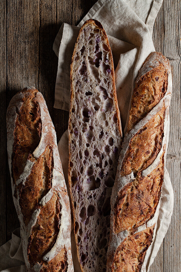 Top view of cut and whole sourdough baguettes with crunchy crust placed on wooden table