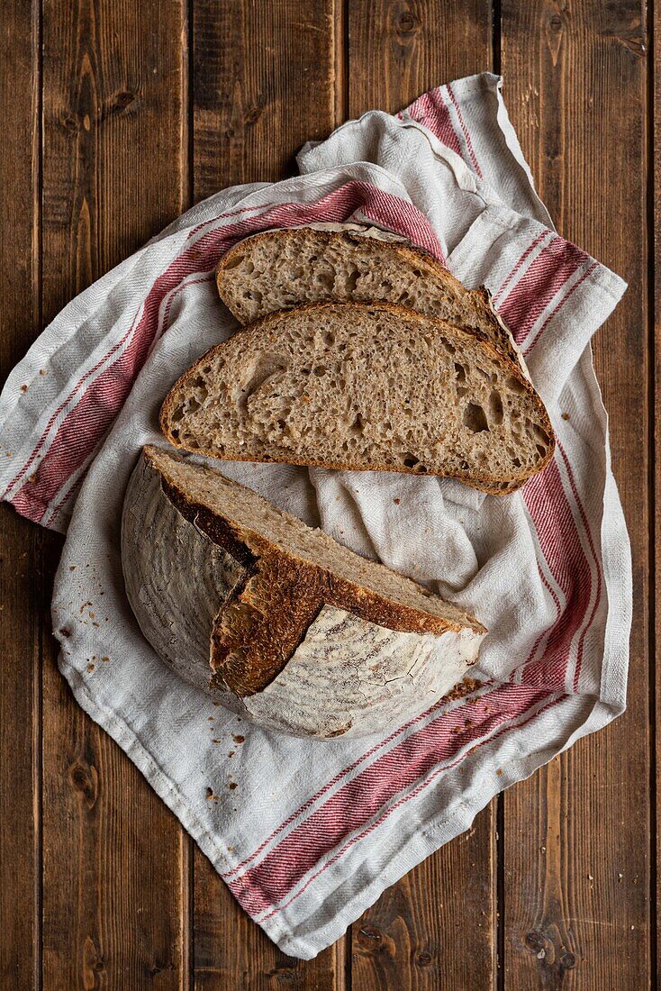 Top view of cut half of sourdough rye bread and slices on towel on wooden rustic table