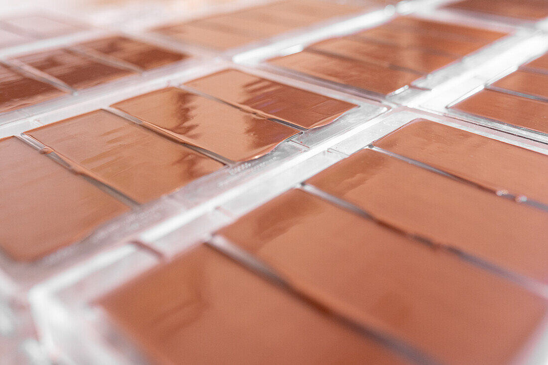 Soft focus of plastic molds with bars of handmade chocolate placed on table in confectionery