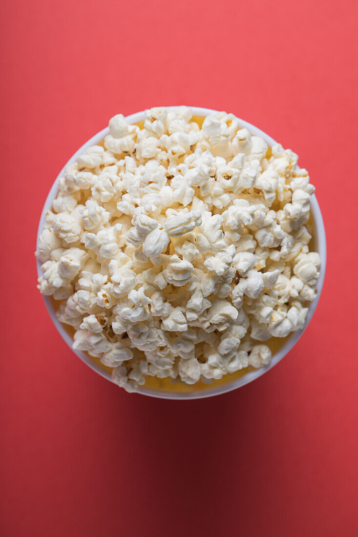 Top view bowl full of popcorn on a red background