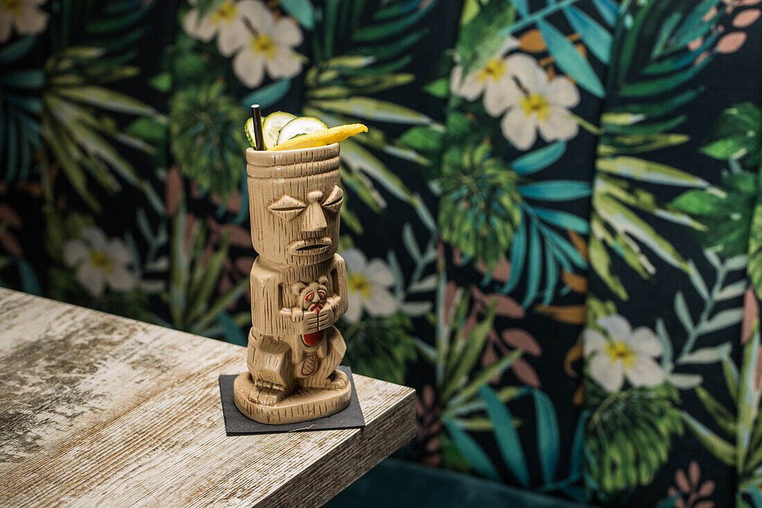 Traditionelle skulpturale Tiki-Tasse mit alkoholischem Getränk und Strohhalm auf einem Holztisch