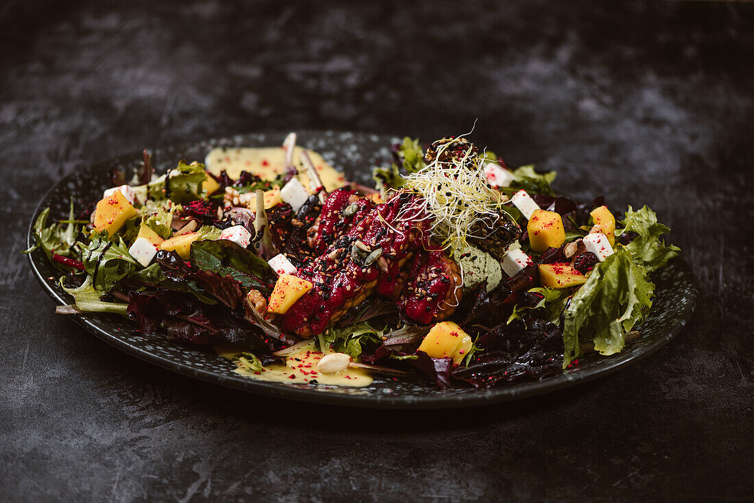 Plate with tasty vegetarian Indonesian salad with fresh mango and cashew cheese slices near soybeans and condiments covered with basil vinaigrette