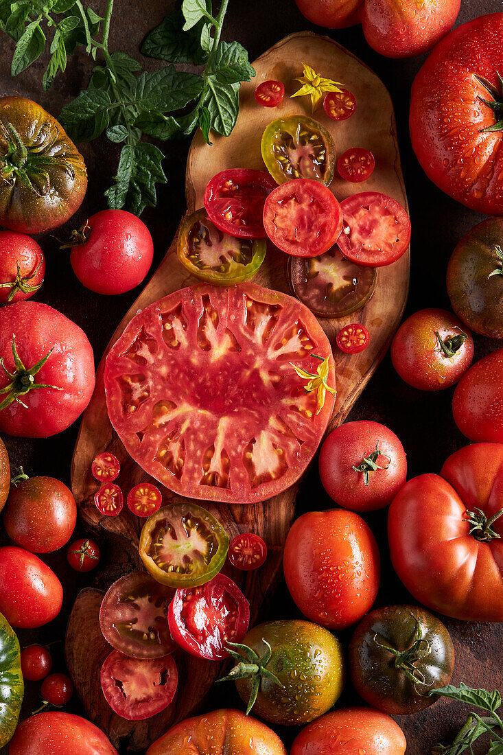 Hochformatige geschnittene Tomate mit Salz auf einem hölzernen Schneidebrett zwischen reifen roten Tomaten mit Wassertropfen