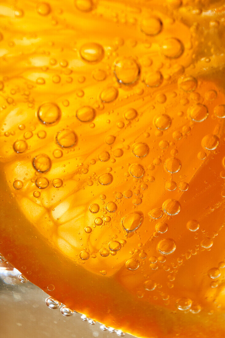 Close-up gin and tonic cocktail with slice of fresh orange bubbling in glass