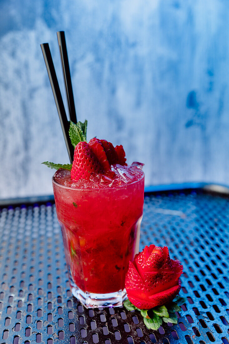Transparentes Glas mit Erdbeer-Mojito-Cocktail aus weißem Rum, Sodawasser und Minzblättern mit Strohhalm