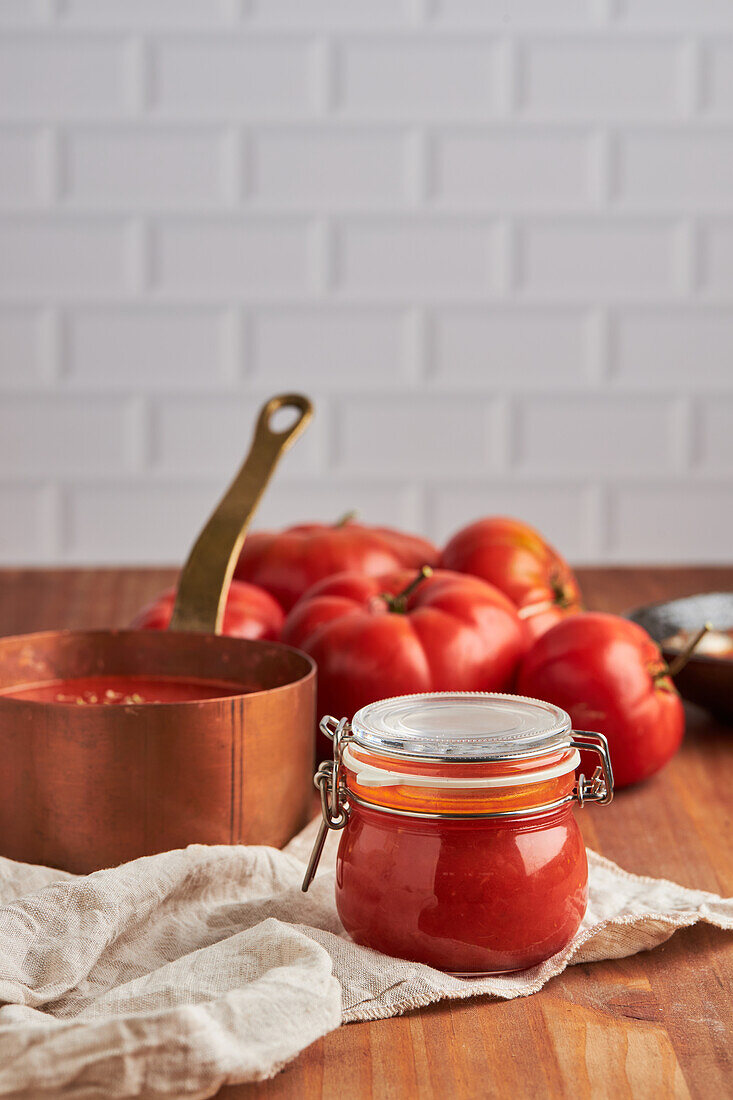 Glass jar with fresh tomato sauce placed on woven mat in kitchen at home
