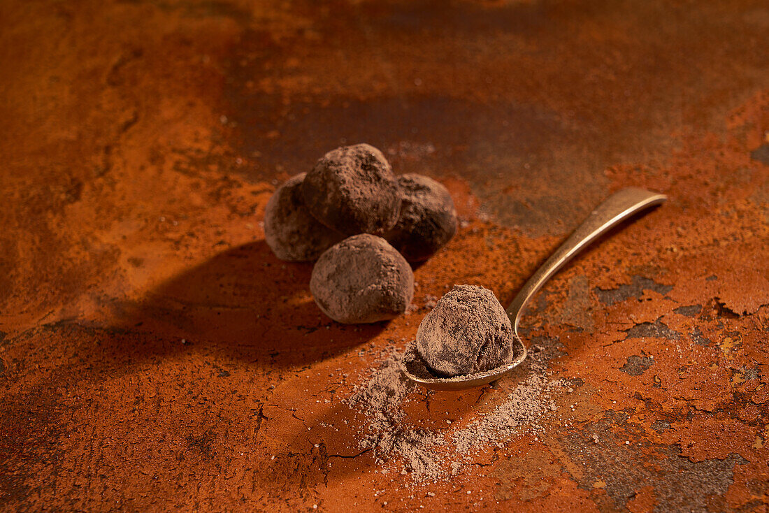 Komposition von oben auf kleinen Metalllöffel mit köstlichen Schokoladentrüffeln und Kakaopulver auf rostiger Oberfläche