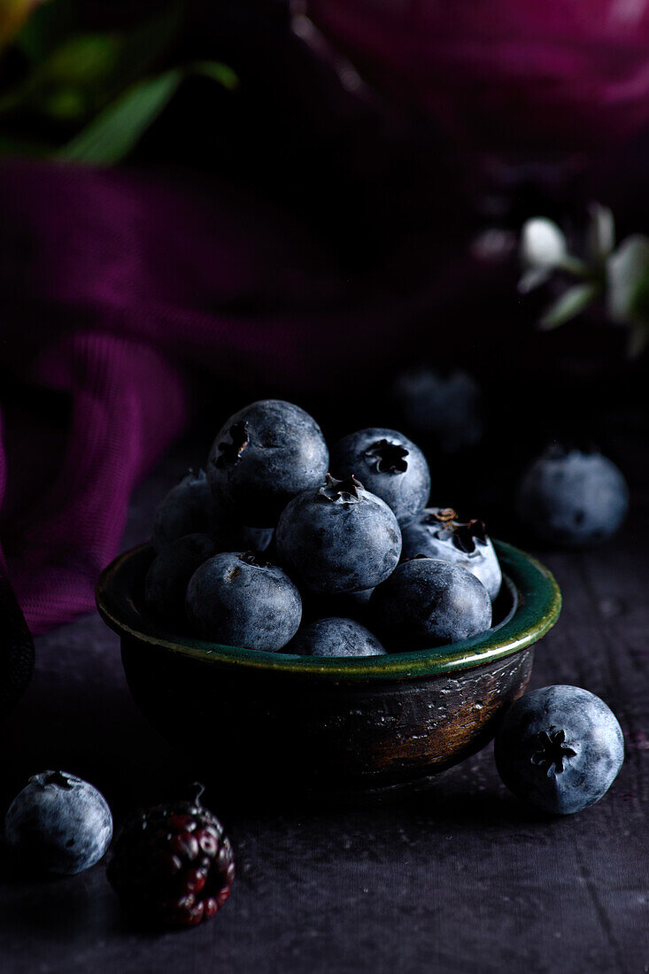 Closeup of pile of ripe blueberries in bowl served on black table with purple cloth