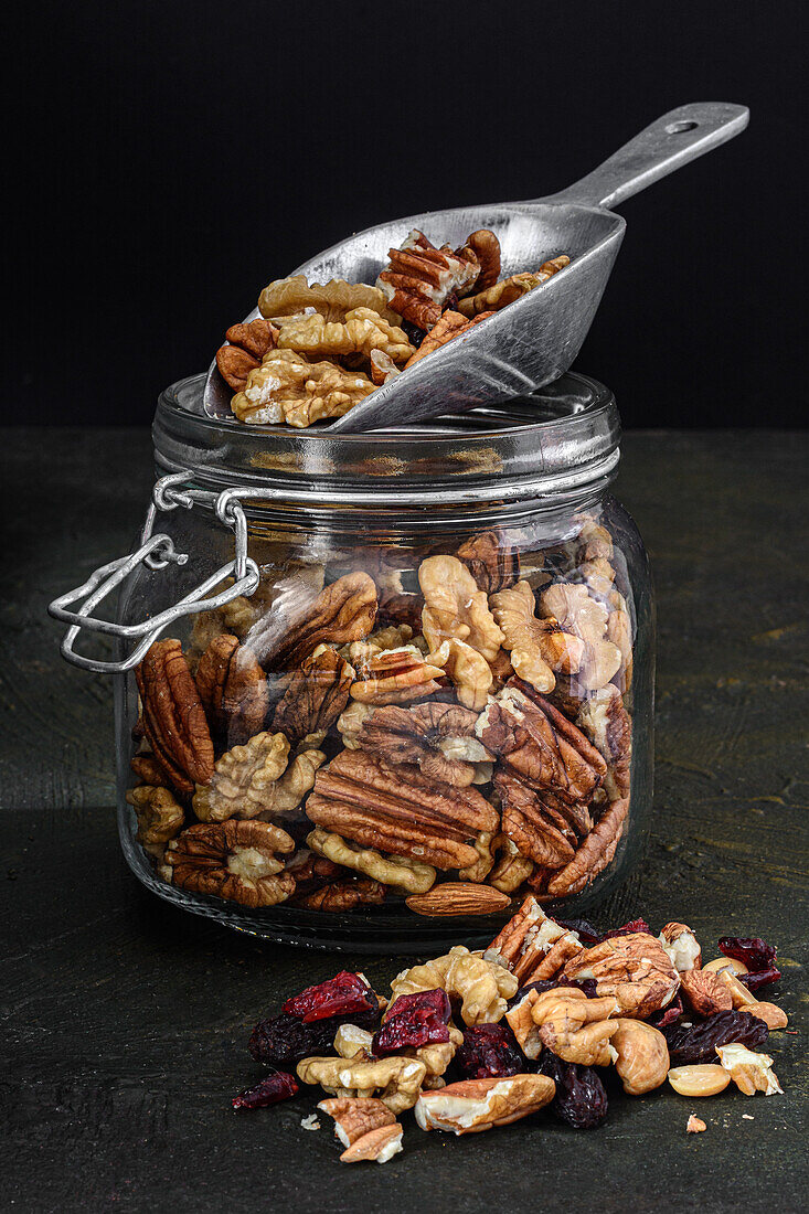 Glasgefäß mit Nüssen und Trockenfrüchten vor dunklem, rustikalem Hintergrund