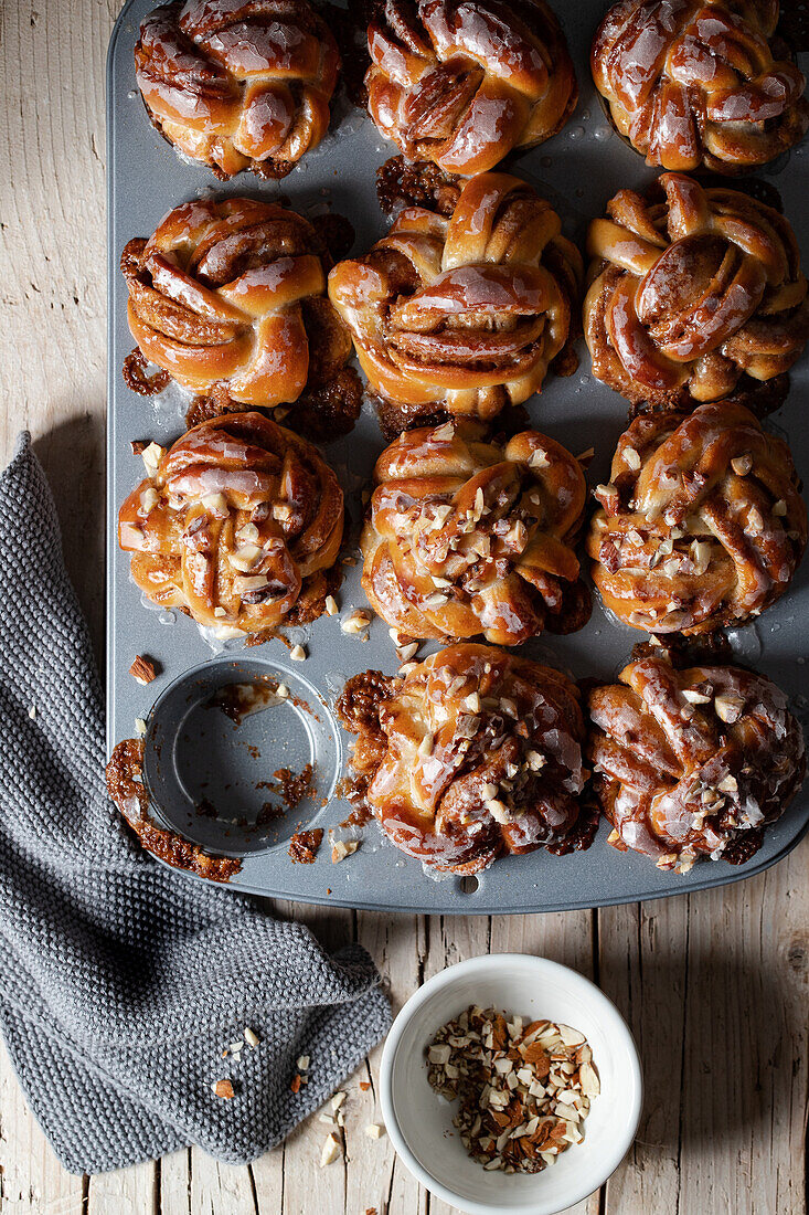 Top view pile of tasty freshly baked homemade cinnamon buns placed on wooden table with ground nuts in light kitchen