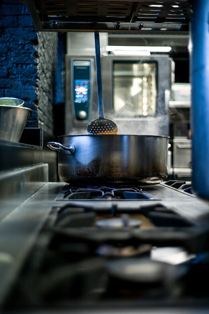 Stahlpfanne mit kochendem Wasser und Dampf auf einem Gasherd in einer Restaurantküche