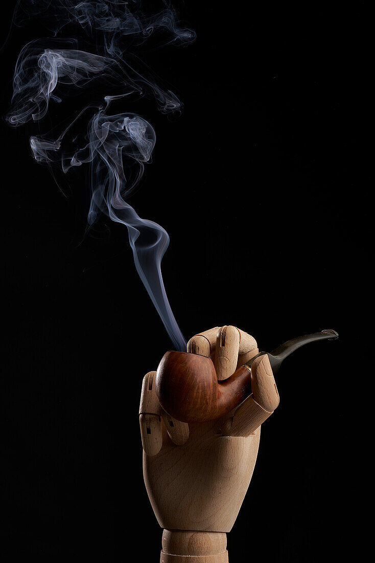 Traditional tobacco pipe with smoke in wooden hand on black background in studio