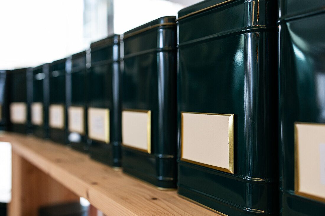 Modern black containers placed in row on wooden shelf in shop with blank labels