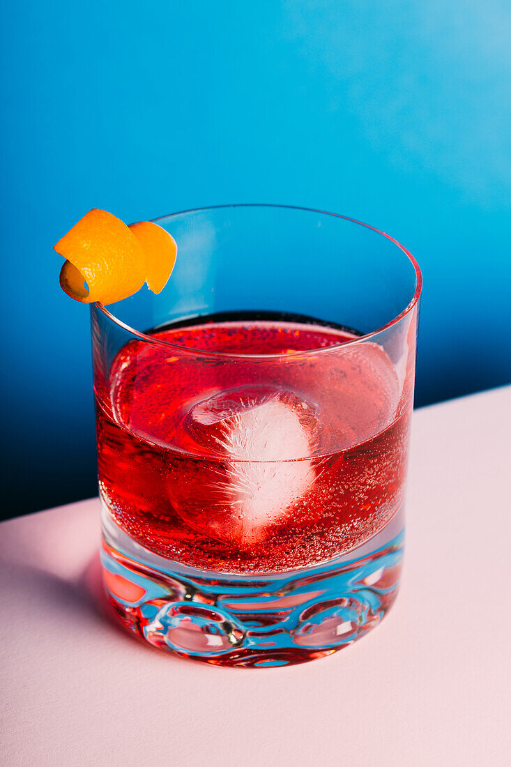Glass of bitter alcoholic Negroni cocktail served with ice and orange peel on light surface