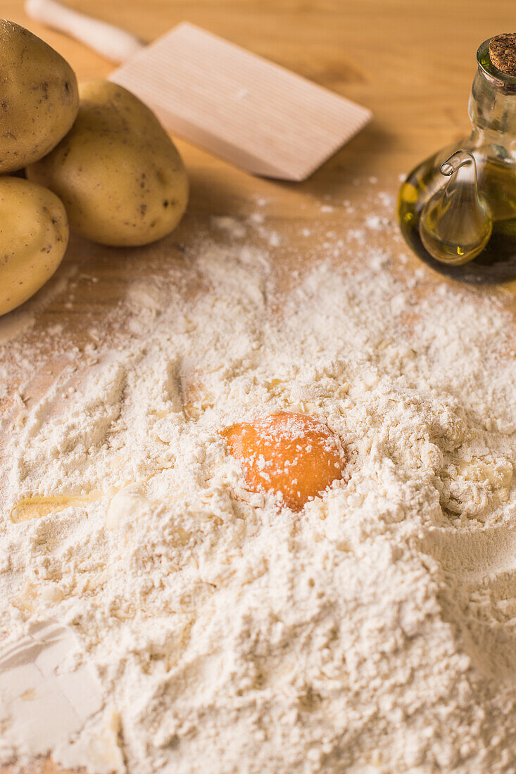 Von oben Eigelb auf einem Haufen Weizenmehl neben Kartoffeln und Öl bei der Zubereitung von Gnocchi-Teig auf einem Tisch in der Küche