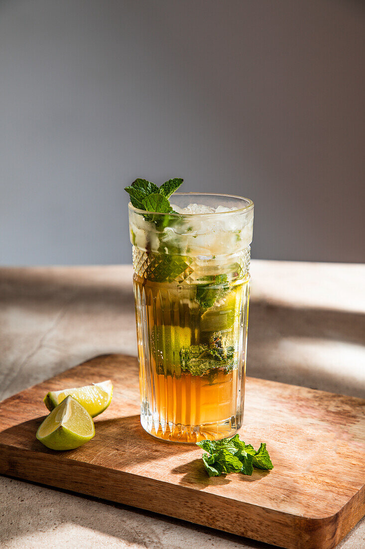 Refreshing cold alcoholic mojito with ice mint leaves and cut lime on wooden board