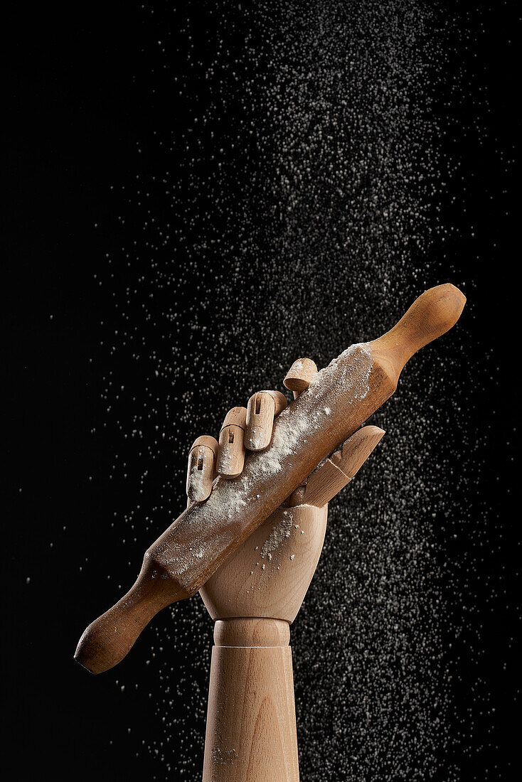 Nudelholz in Mehl in einer hölzernen Hand auf schwarzem Hintergrund in einem Studio, das ein kulinarisches Konzept zeigt