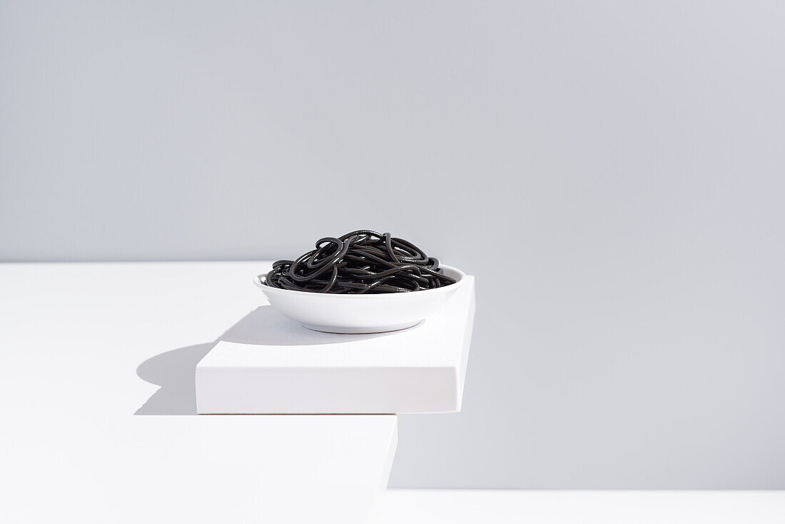 Minimalist studio with black squid ink spaghetti in full ceramic bowl on white table