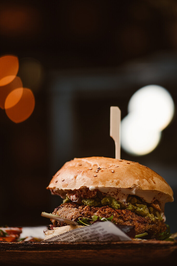 Niedriger Winkel eines leckeren Burgers mit vegetarischem Patty und gegrillten Shiitakes zwischen Brötchen neben Süßkartoffel- und Karottenscheiben mit Alioli-Sauce auf dunklem Hintergrund