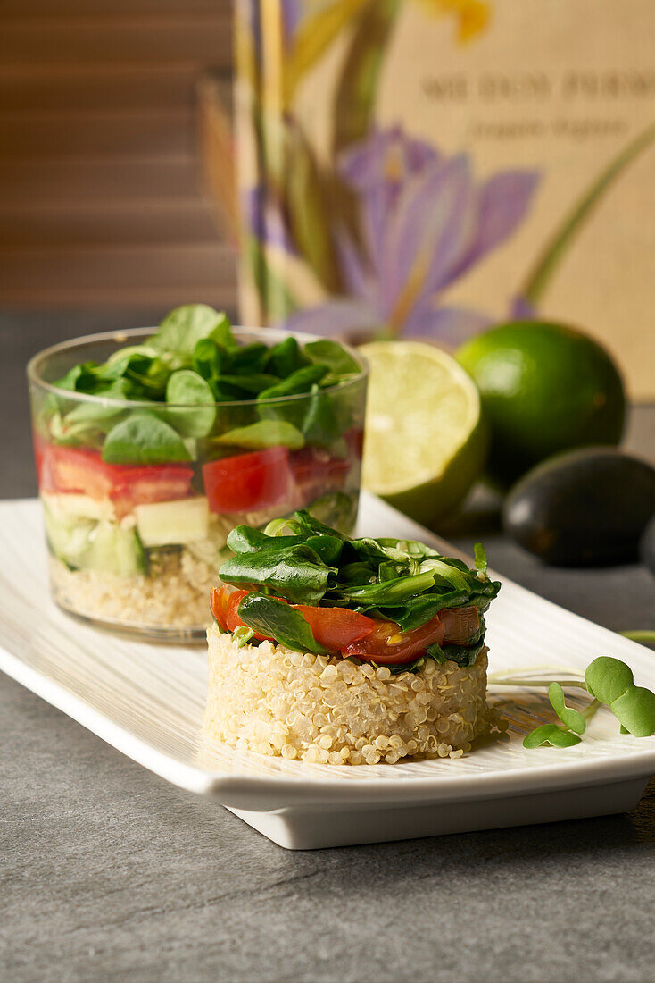 Blick von oben auf einen leckeren Salat aus Reis und Gemüse in runder Form und im Glas serviert auf einem weißen Teller neben grünen Limetten auf einem grauen Tisch