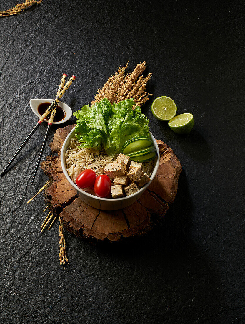 From above of bowl with fresh tomato tofu and sprouts placed on wooden board near lime on black table