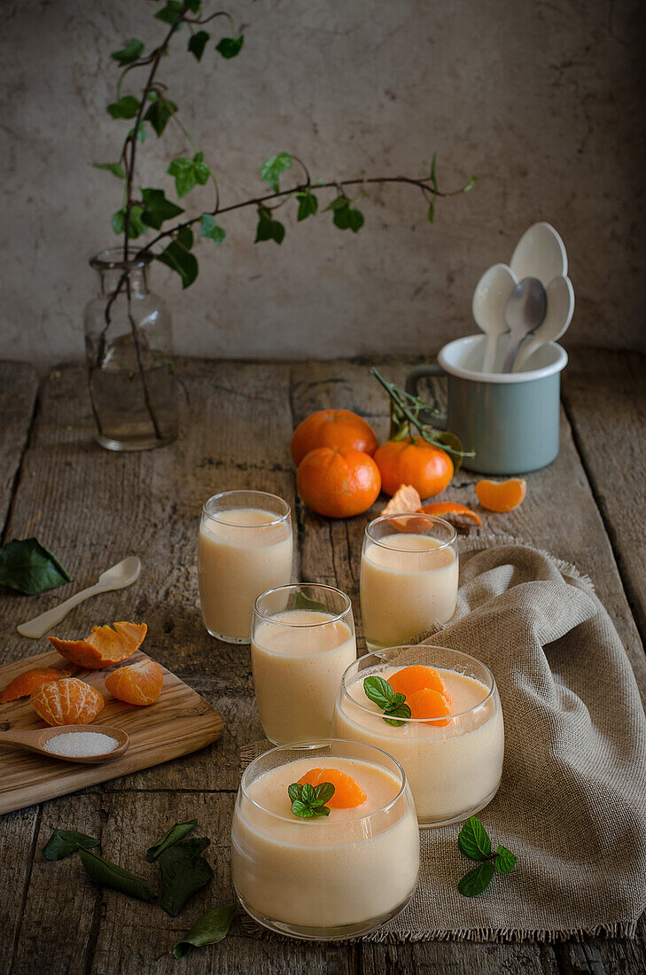 Blick von oben auf eine leckere Mandarinenmousse, garniert mit frischen Minzblättern, serviert in Glasbechern auf einem Holztisch