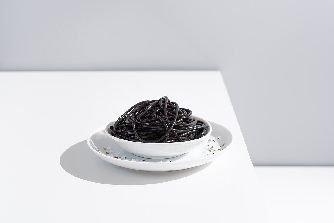 Minimalist studio with black squid ink spaghetti in full ceramic bowl on white table