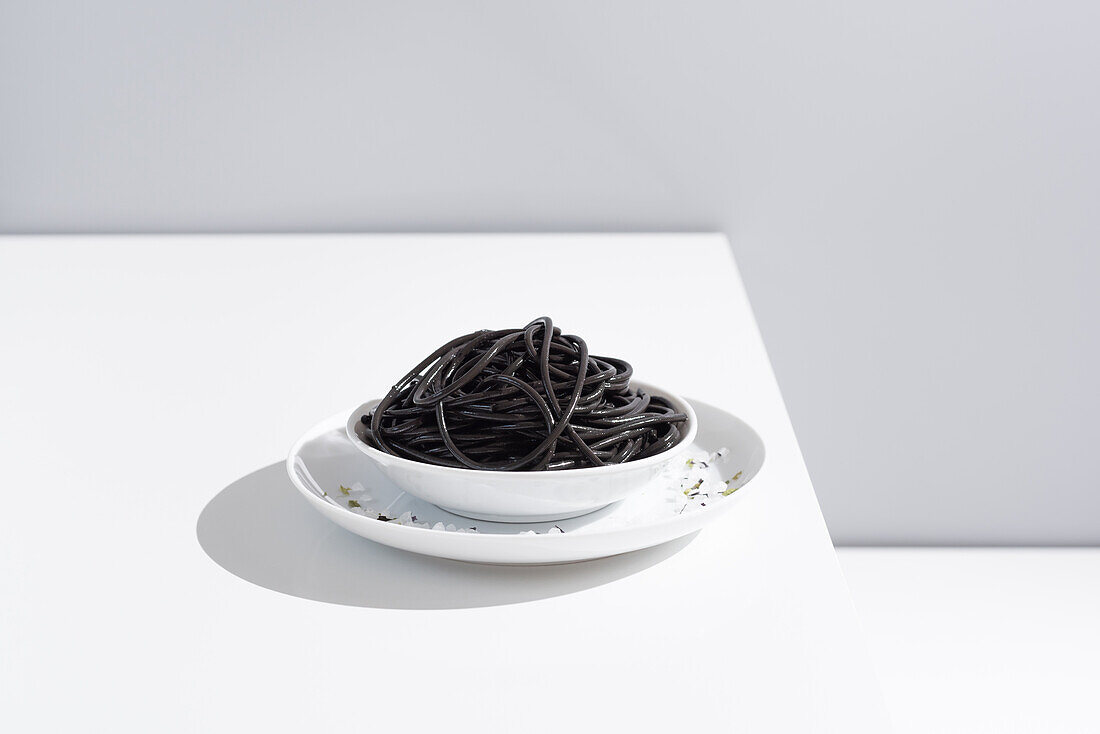 Minimalistisches Studio mit schwarzen Tintenfischspaghetti in einer vollen Keramikschale auf einem weißen Tisch