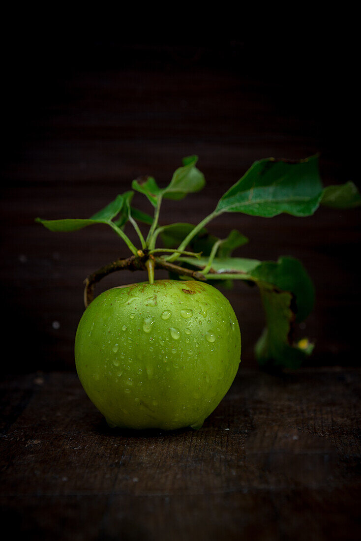 Whole ripe green apple with foliage and pure small aqua drips on black background